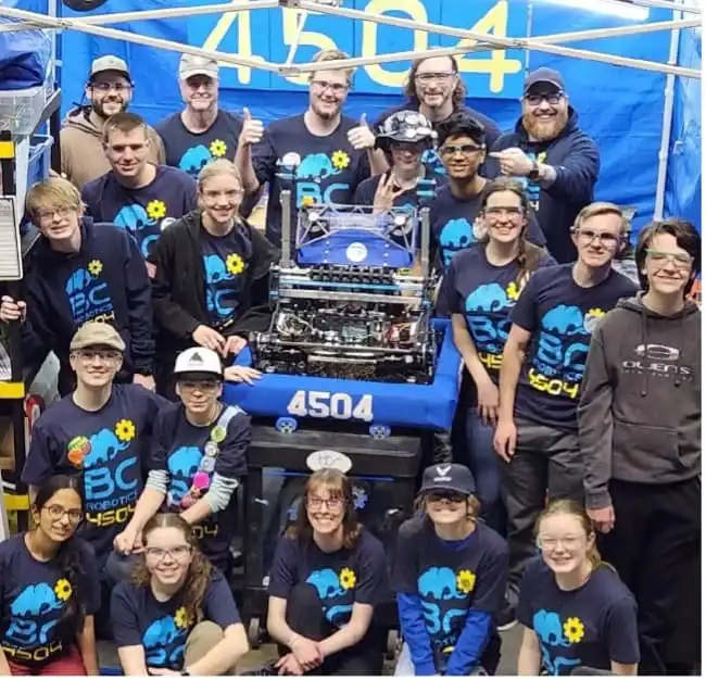Team of students and mentors with their robotics vehicle at a STEM event.