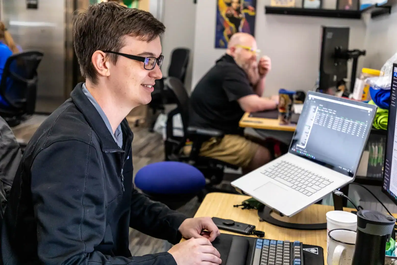 Young man working on a laptop in a tech office environment.