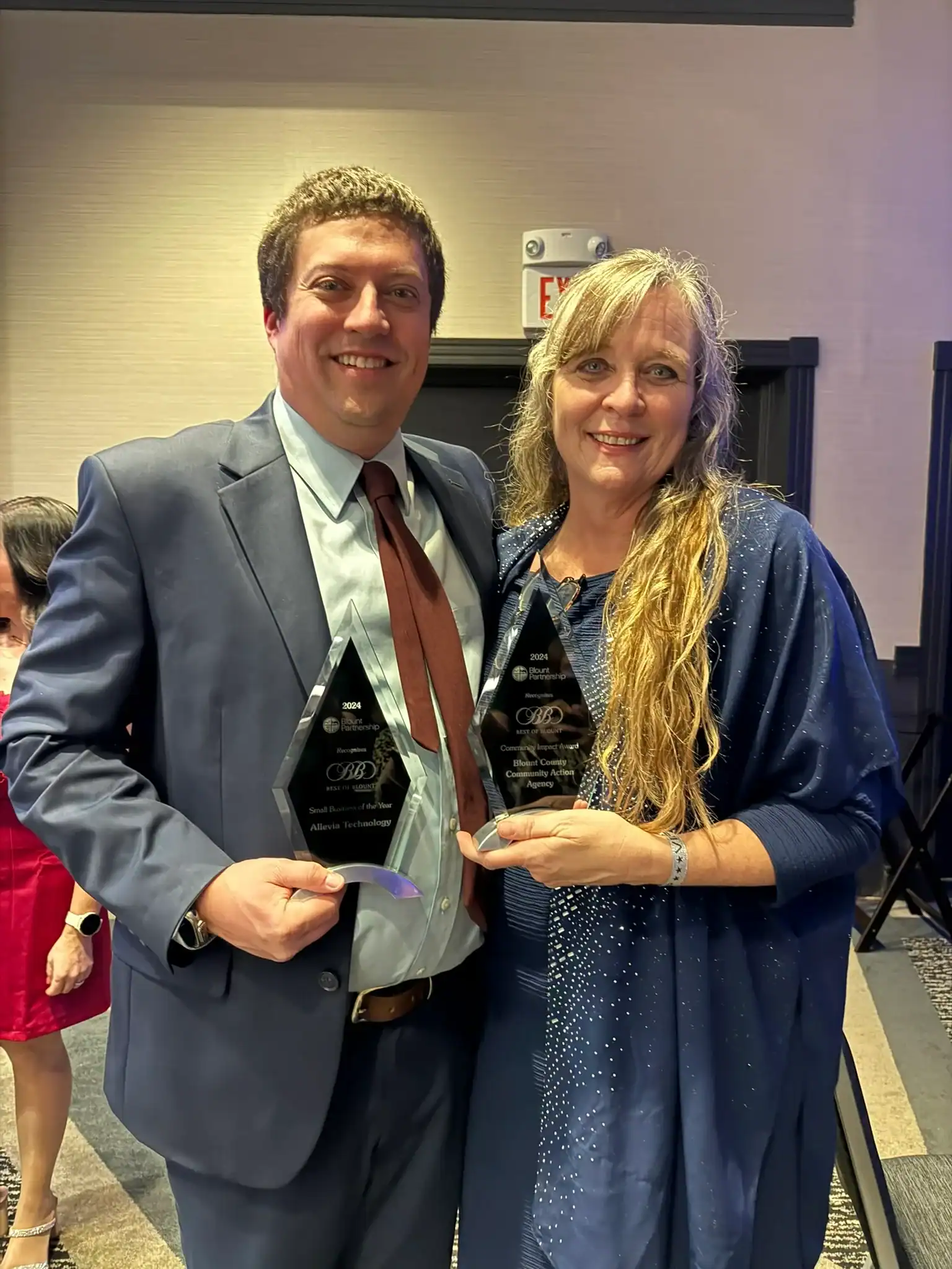 Two professionals holding awards at a corporate event in a conference room.