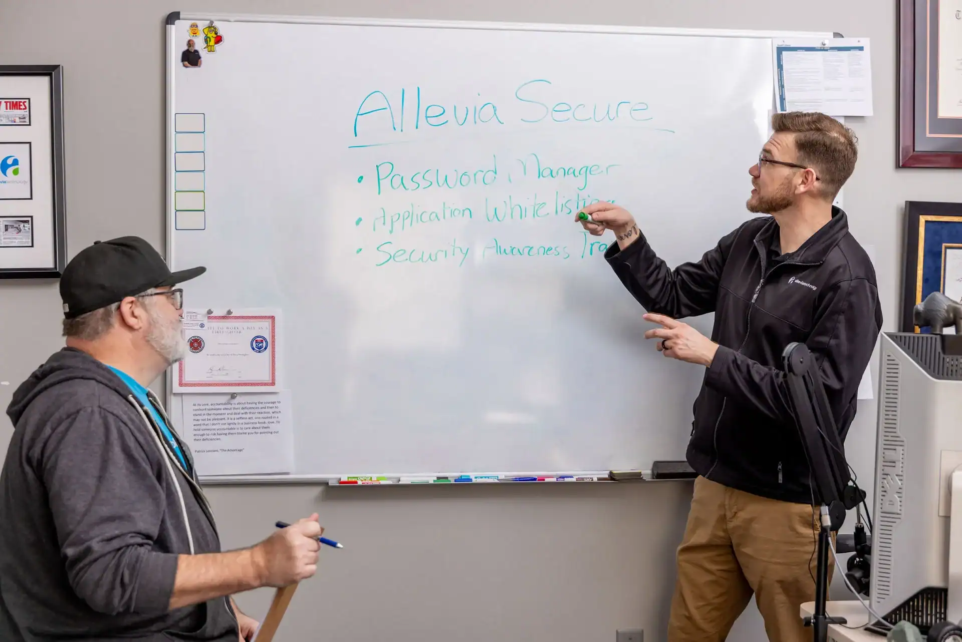 Two men discussing cybersecurity on a whiteboard in an office setting.