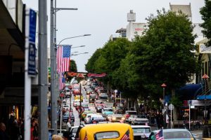 Classic American cars parade on busy street in Australia, celebrating automotive culture.
