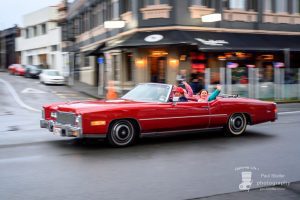 Red vintage Cadillac convertible cruising city street in New Zealand.