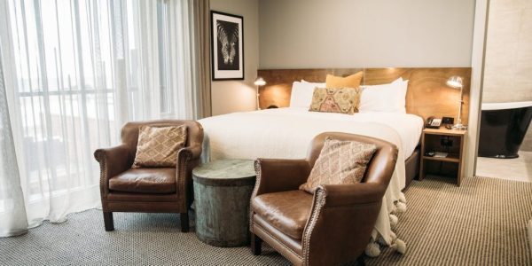 Luxurious hotel room with comfortable bed, leather chairs, and modern decor in a stylish setting.