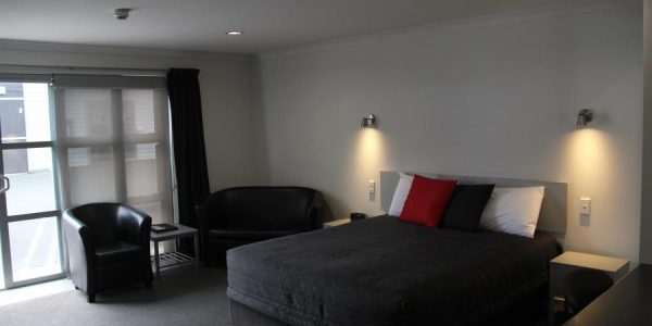 Comfortable hotel room with modern decor, black leather seating, and a cosy bed in New Zealand.