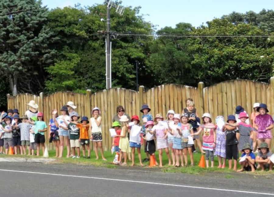 Children waiting in a line along the roadside, participating in a community event or parade.