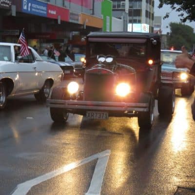Classic American cars parade on wet city street during Americarna event.
