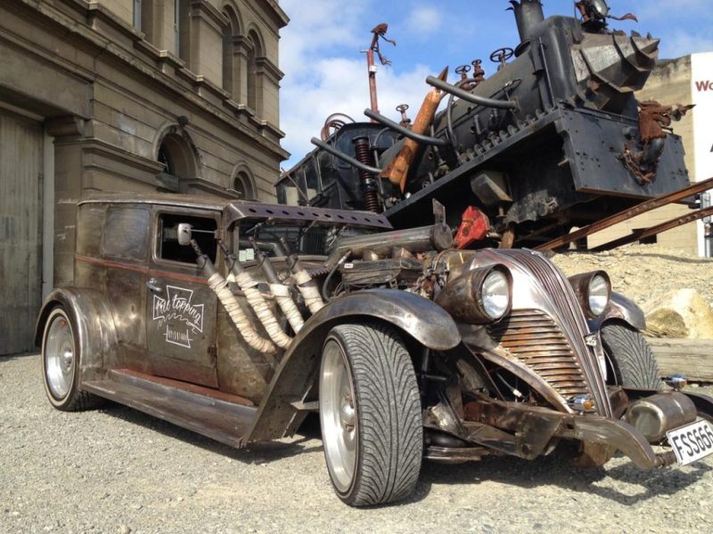 Rustic vintage-style custom car with unique engine art in urban setting.