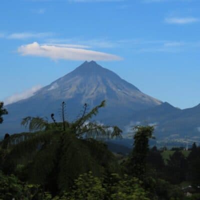 Vulcán en Nueva Zelanda con nubes en el cielo y vegetación en primer plano.