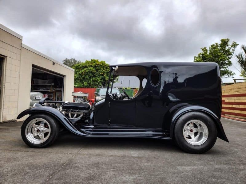 Vintage black hot rod car parked in drive with classic design and chrome wheels.