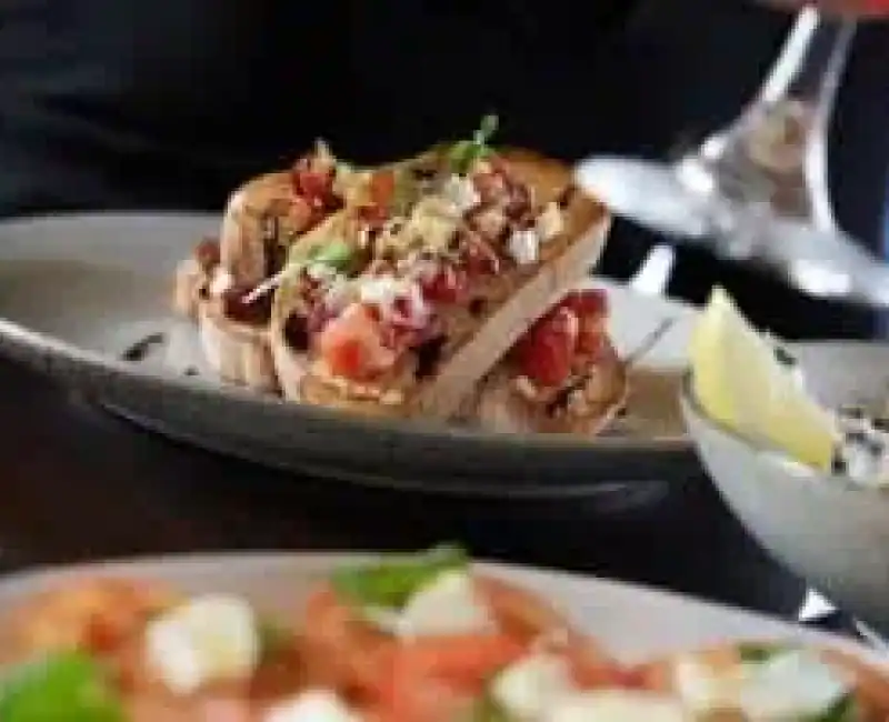 Delicious gourmet hot dog topped with fresh ingredients, served on a black plate for a gourmet dining experience.