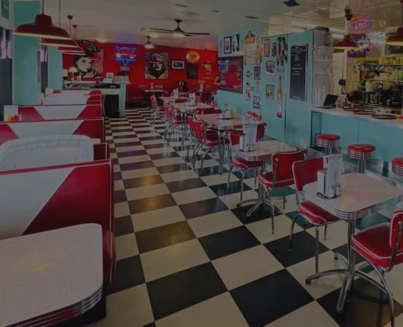 Interior of classic American diner with red chairs, checkered floor, and vintage wall art.