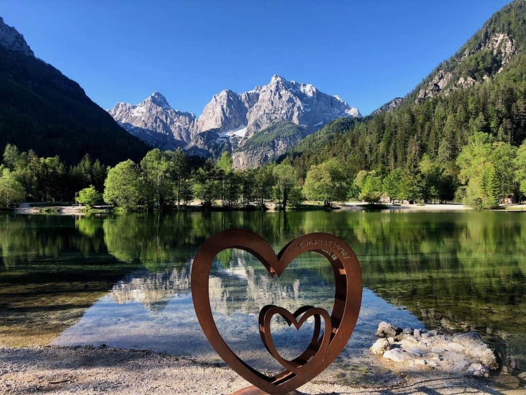 a heart shaped sculpture by a lake with mountains in the background