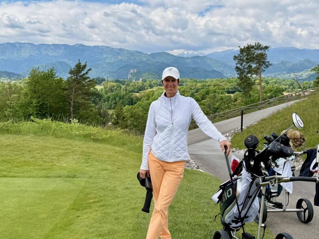 a woman on a golf course with trees and mountains in the background