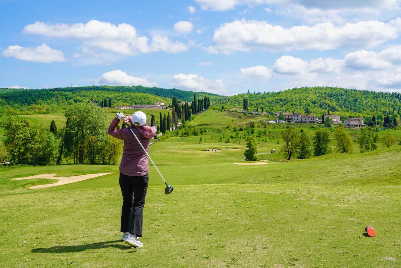Woman playing golf on a lush green course with scenic hills in the background.