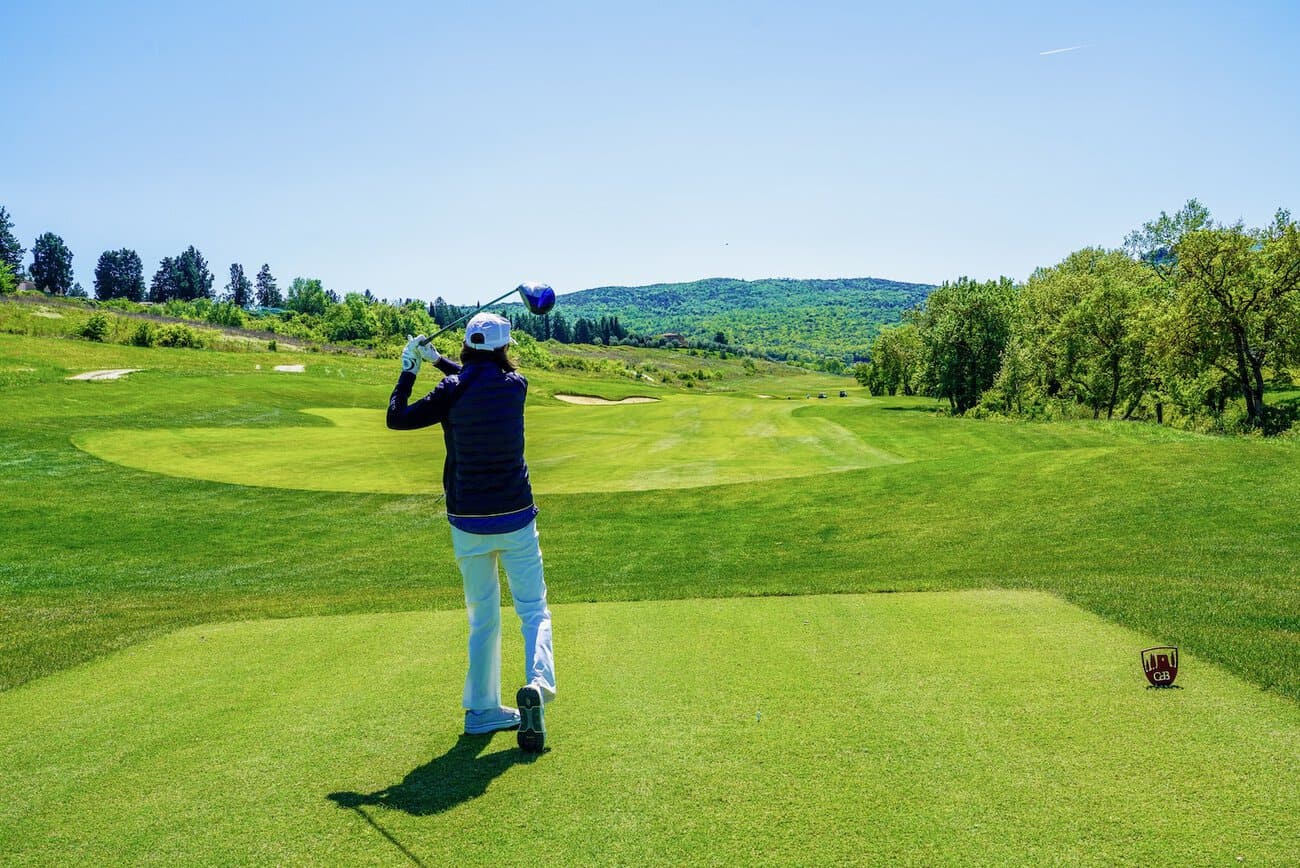 Golfer taking a swing on a lush green golf course with scenic hills in the background.