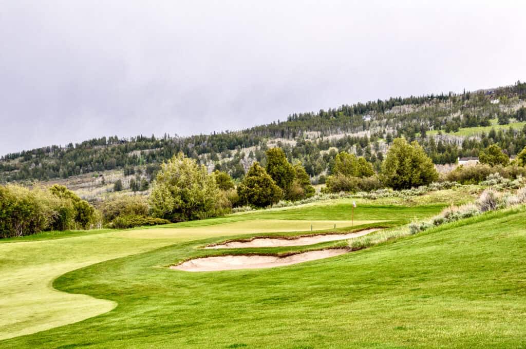 Scenic golf course with sand traps and lush green fairways under cloudy sky.