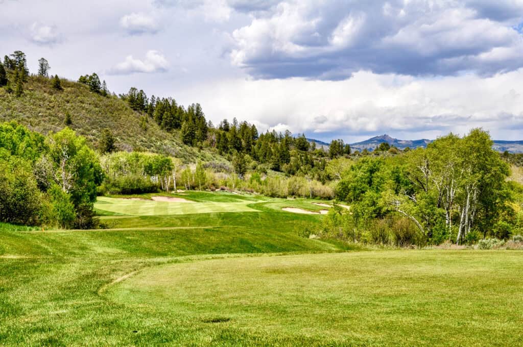 Scenic view of a lush green golf course with rolling hills and trees under a partly cloudy sky.