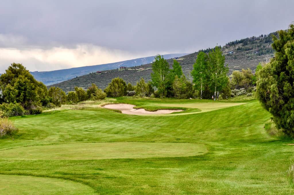 Scenic golf course with lush green fairways and sand traps under cloudy sky.