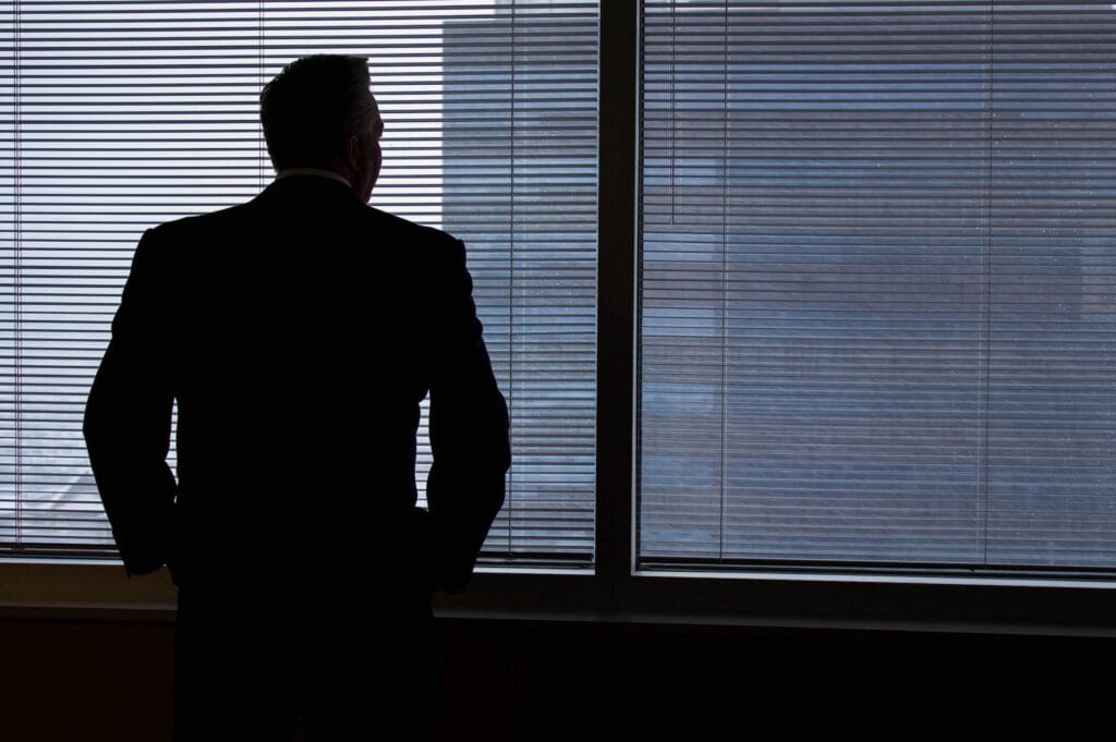 Silhouette d’un homme d’affaires regardant par une fenêtre avec des stores vénitiens, ambiance professionnelle et élégante.