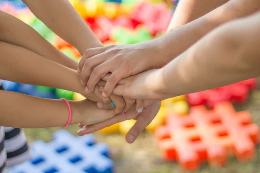 Main en rangée avec plusieurs mains jointes, symbolisant la solidarité et l'esprit d'équipe, devant un fond coloré.
