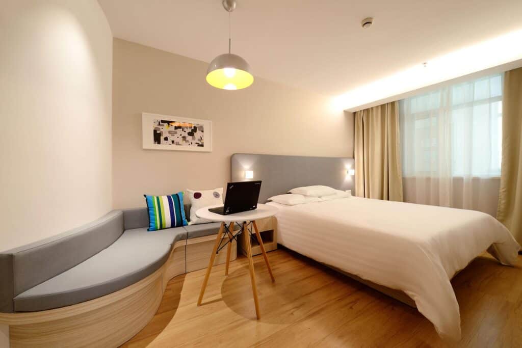 Lit d'hôtel moderne avec coin salon, ordinateur portable, décoration épurée et grande fenêtre avec rideaux, chambre confortable à Montréal.