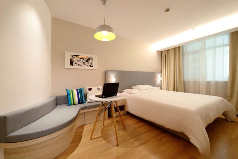 Lit d'hôtel moderne avec coin salon, ordinateur portable, décoration épurée et grande fenêtre avec rideaux, chambre confortable à Montréal.