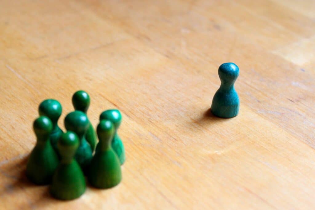 Diffuseur de conflit, guerre ou compétition avec un seul individu isolé face à un groupe de figurines vertes sur une surface en bois.