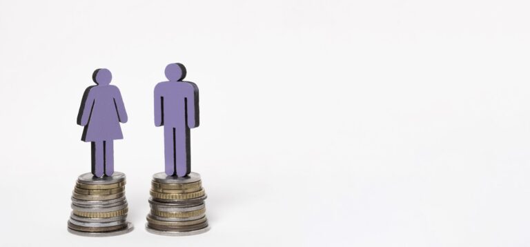 Représentation de symboles de genre masculins et féminins en plastique, placés sur des piles de pièces de monnaie, illustrant l'importance de l'égalité salariale pour 2025.