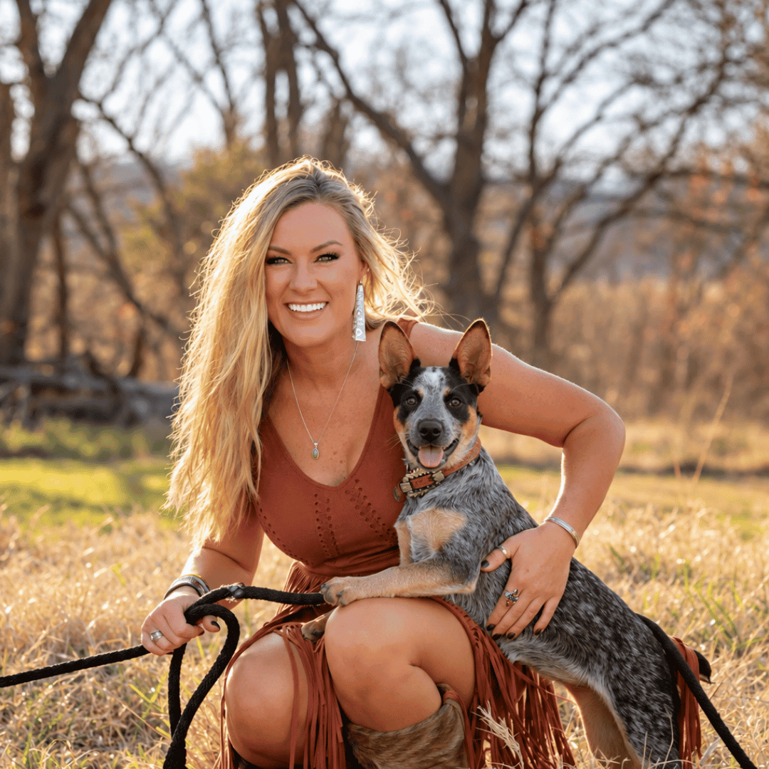 Tricia Phillips kneeling in a field with her blue heeler, Tyra Jean