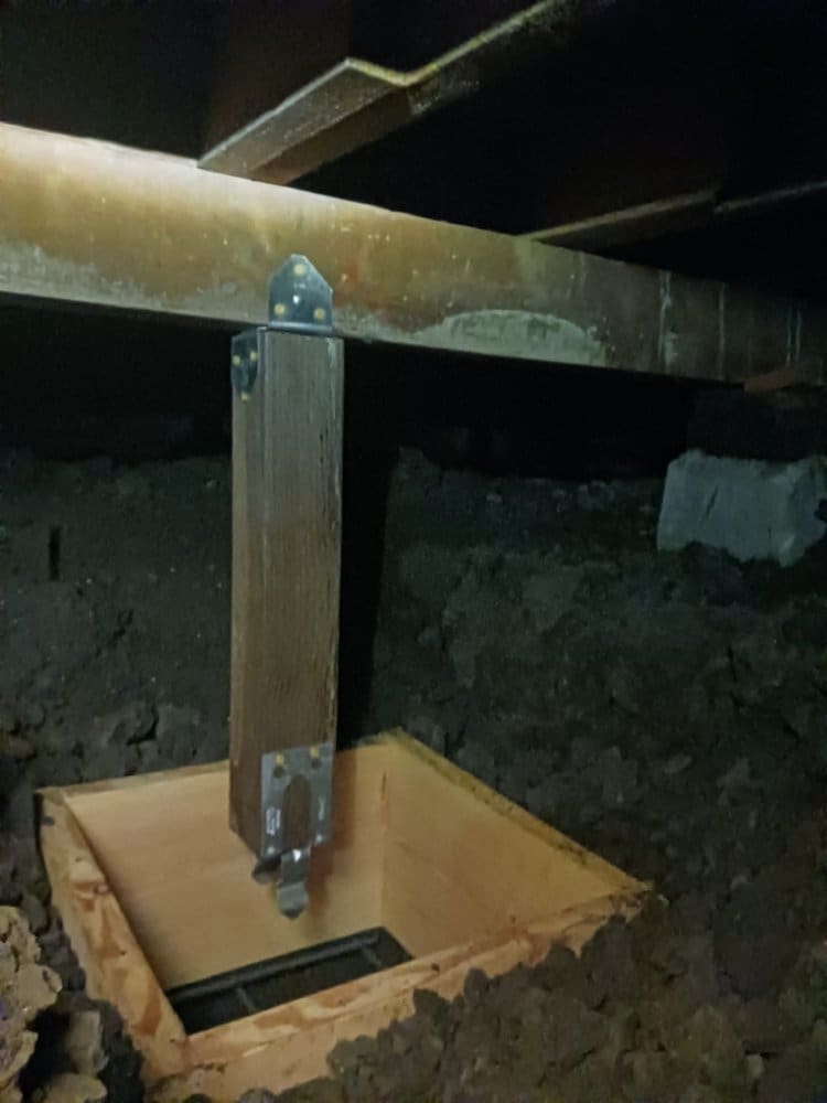 Wooden post supporting a beam in a dark crawl space with an open pit.
