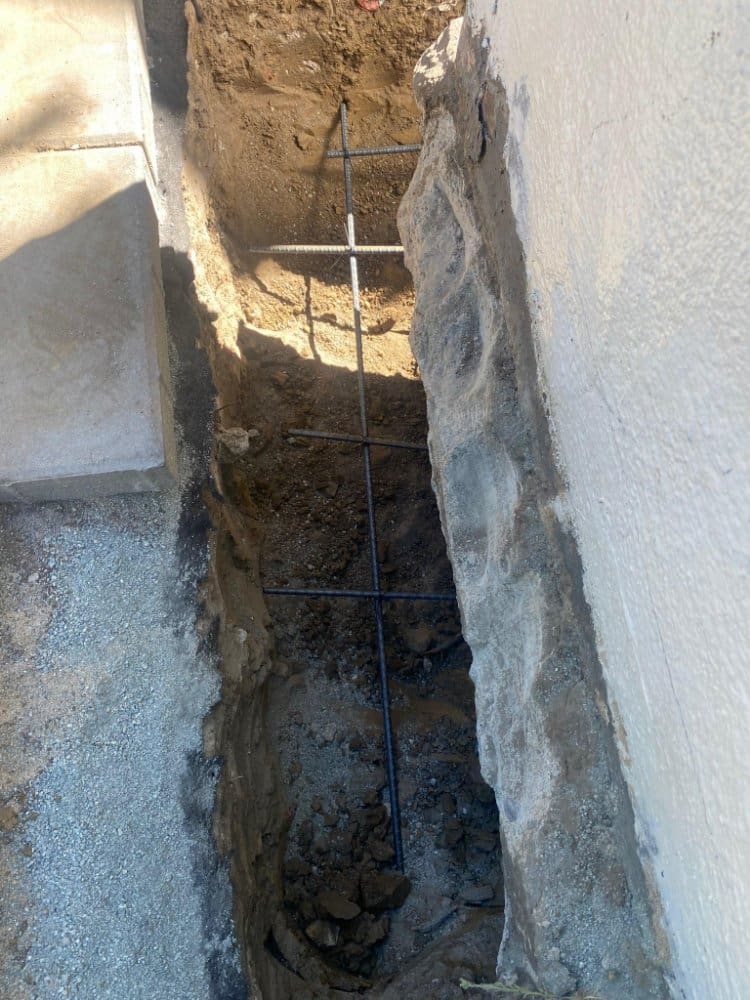 Deep trench with rebar next to a building foundation.