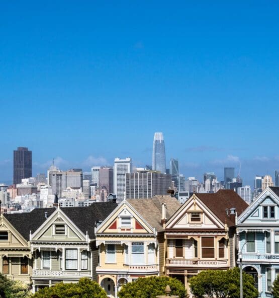 Row of colorful Victorian houses with a city skyline in the background.