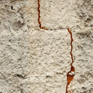 Close-up of a cracked concrete wall with rust stains.