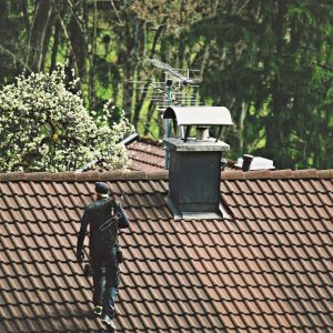 Rooftop Worker on Tiled Roof with Chimney and Antenna Person in dark clothing walking on a tiled roof towards a chimney.