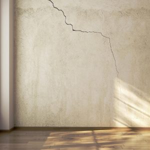 Large crack on a textured beige wall in an empty room with sunlight.