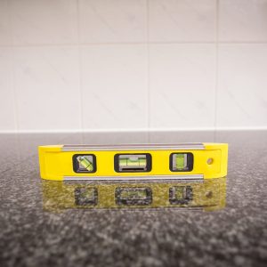 Yellow spirit level on a dark speckled countertop with white tiled wall.