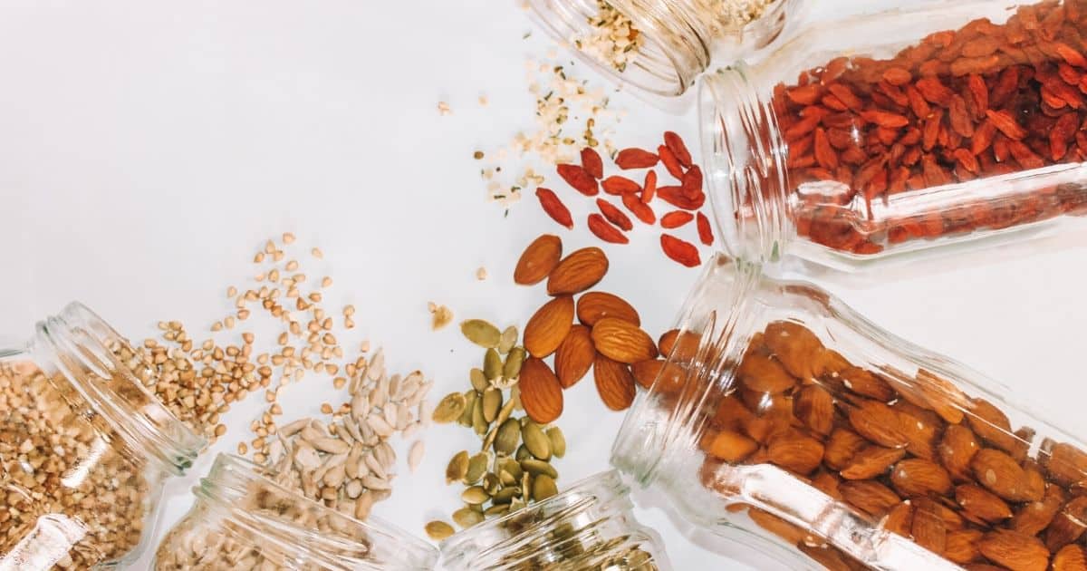 Jars of dried fruit, nuts and grains, on their sides, in a semi circle spilling out contents