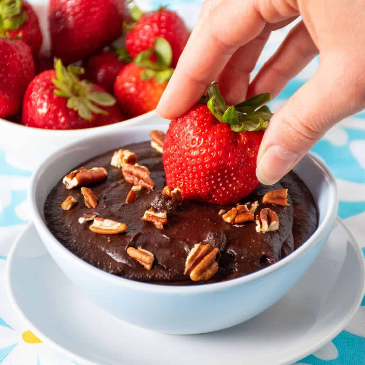 Strawberry being dipped into a bowl of brownie batter dip.