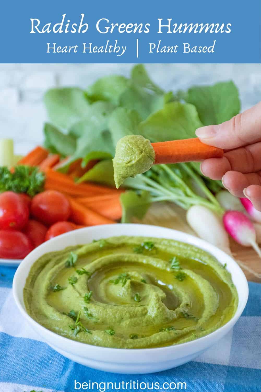 Radish Greens Hummus in a bowl with a hand dipping a carrot stick in it.