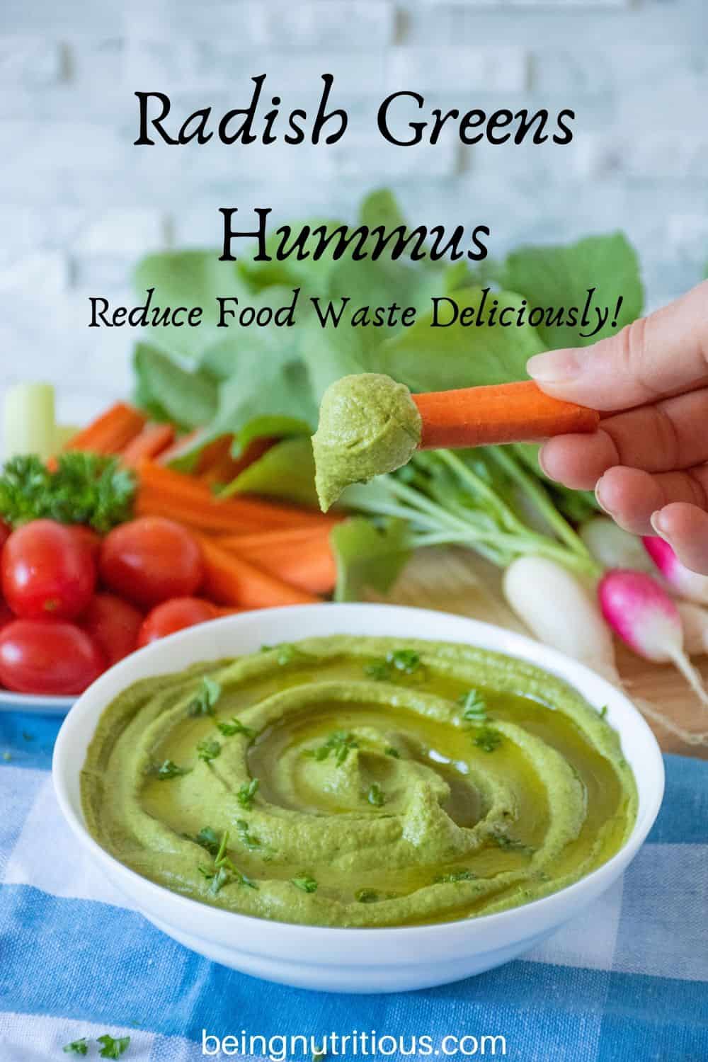Radish Greens Hummus in a bowl with a hand dipping a carrot stick in it.