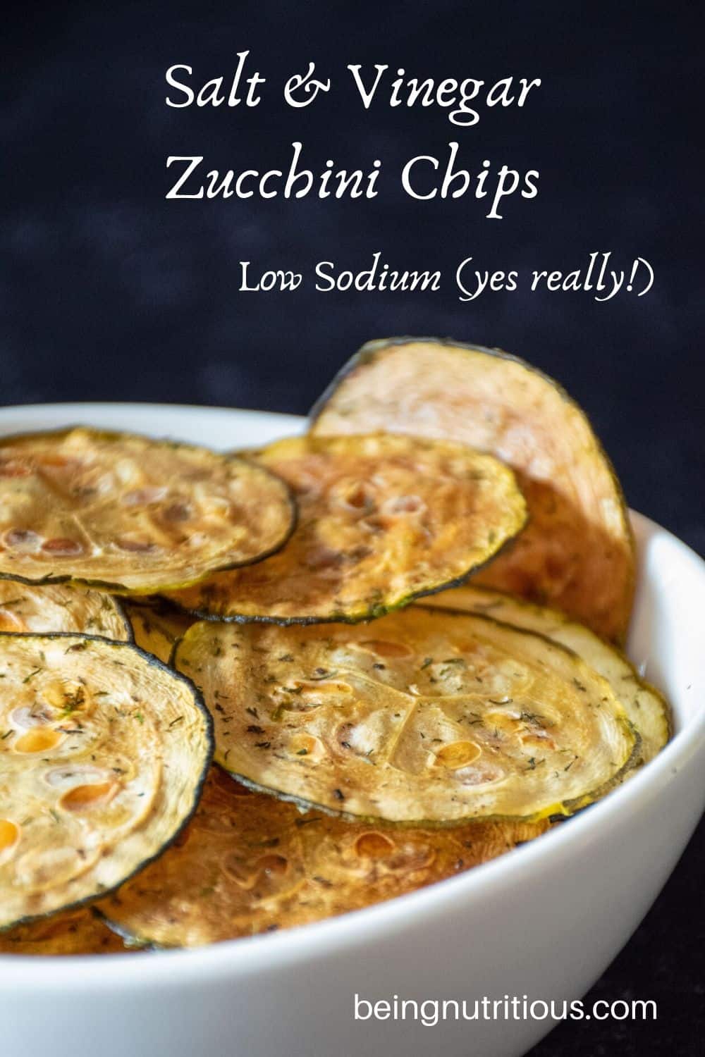 Zucchini chips in a white bowl in front of dark background.