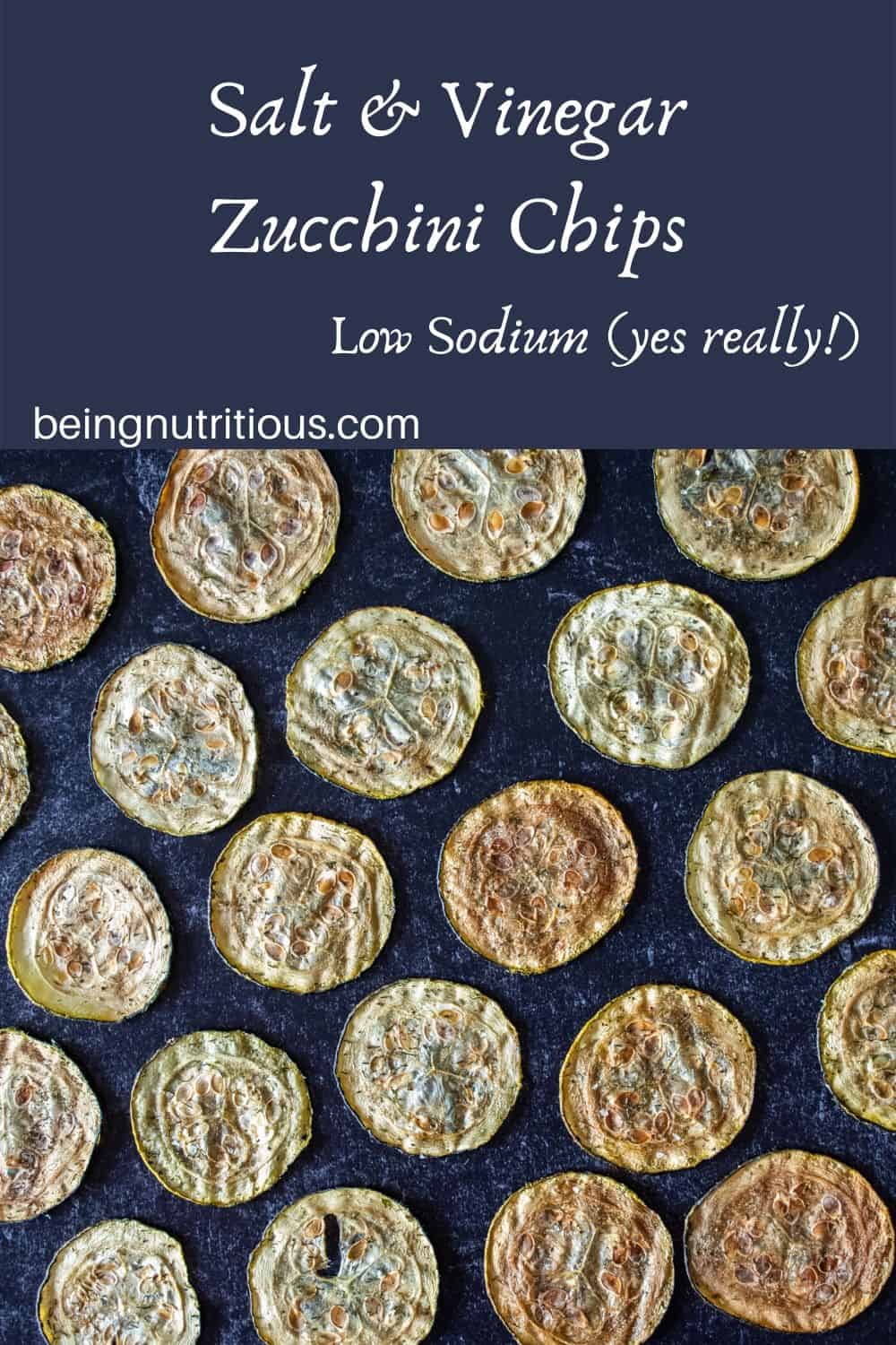 Overhead shot of zucchini chips arranged on a dark background, in a single layer, equidistant apart.