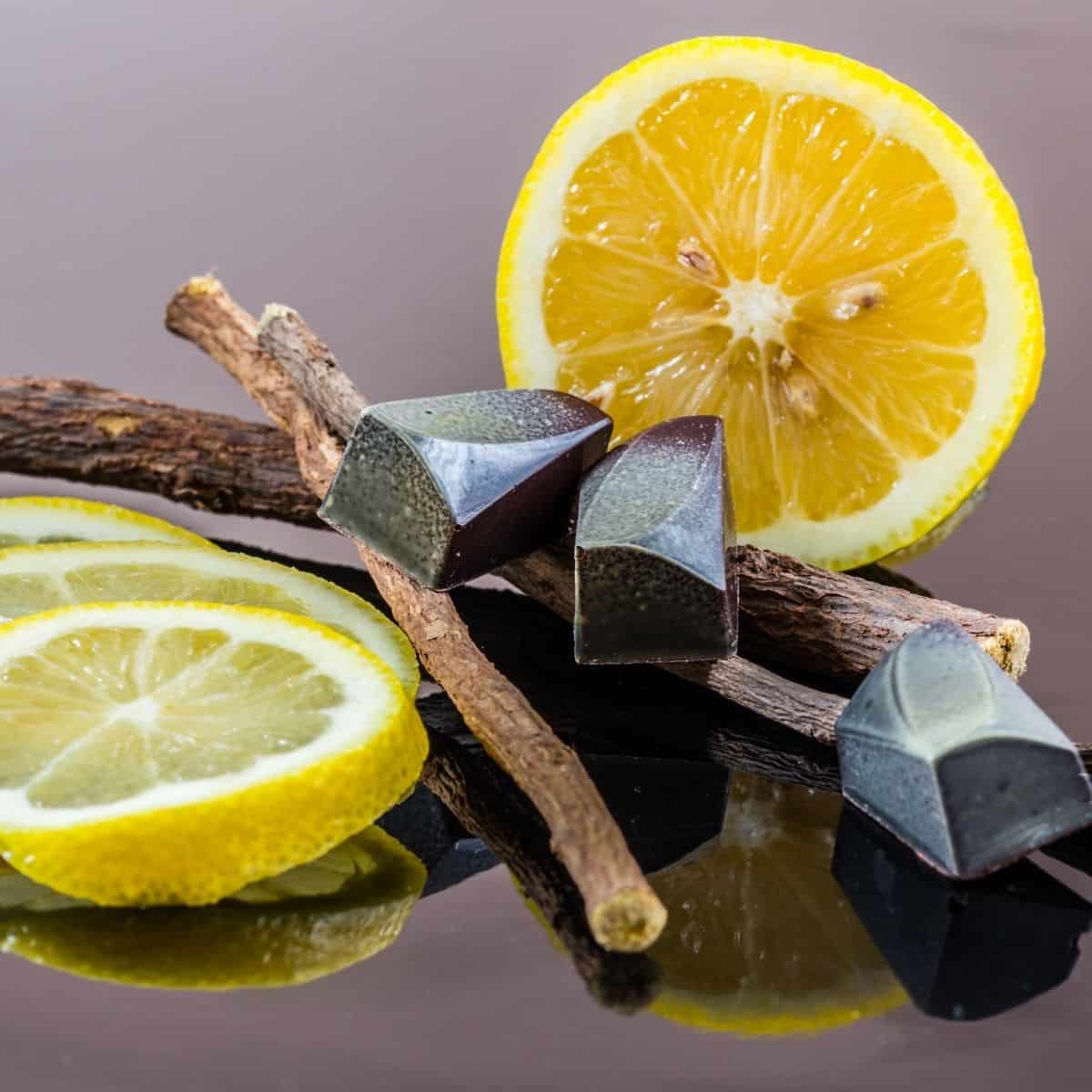 Black licorice candies sitting on licorice root, with lemon slices behind.