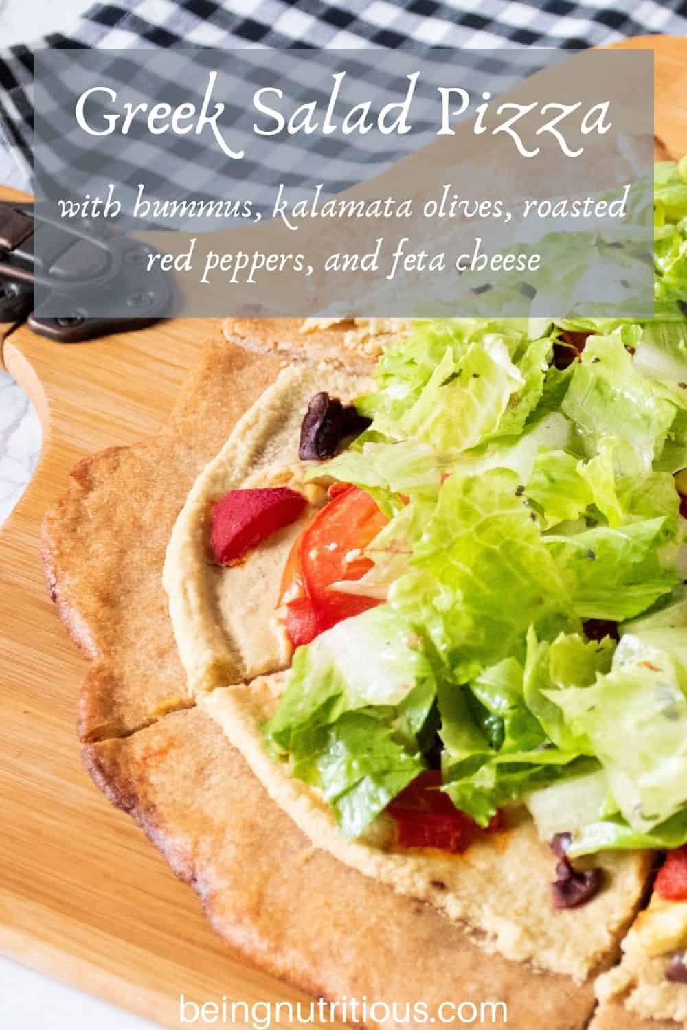 Pizza on a peel, with whole wheat crust, topped with salad. Text overlay: Greek Salad Pizza with hummus, kalamata olives, roasted red peppers, and feta cheese.