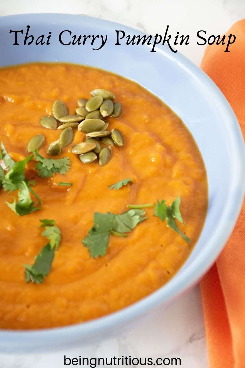 Overhead shot of pumpkin soup in a blue bowl, garnished with cilantro and pepitas. Text overlay: Thai Curry Pumpkin Soup