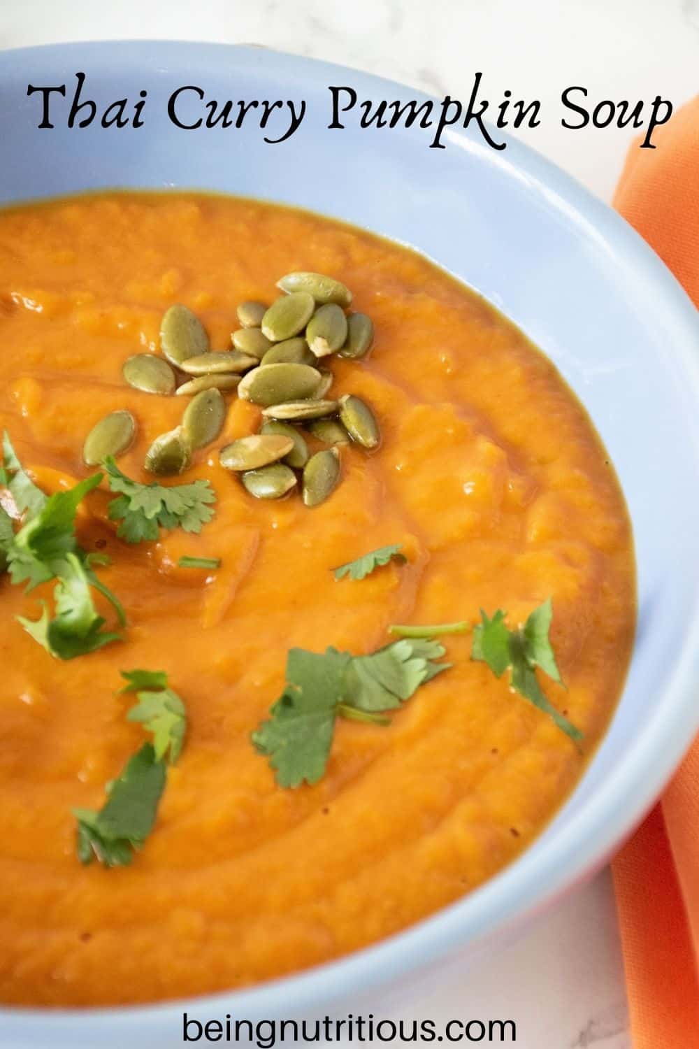 Overhead shot of pumpkin soup in a blue bowl, garnished with cilantro and pepitas. Text overlay: Thai Curry Pumpkin Soup