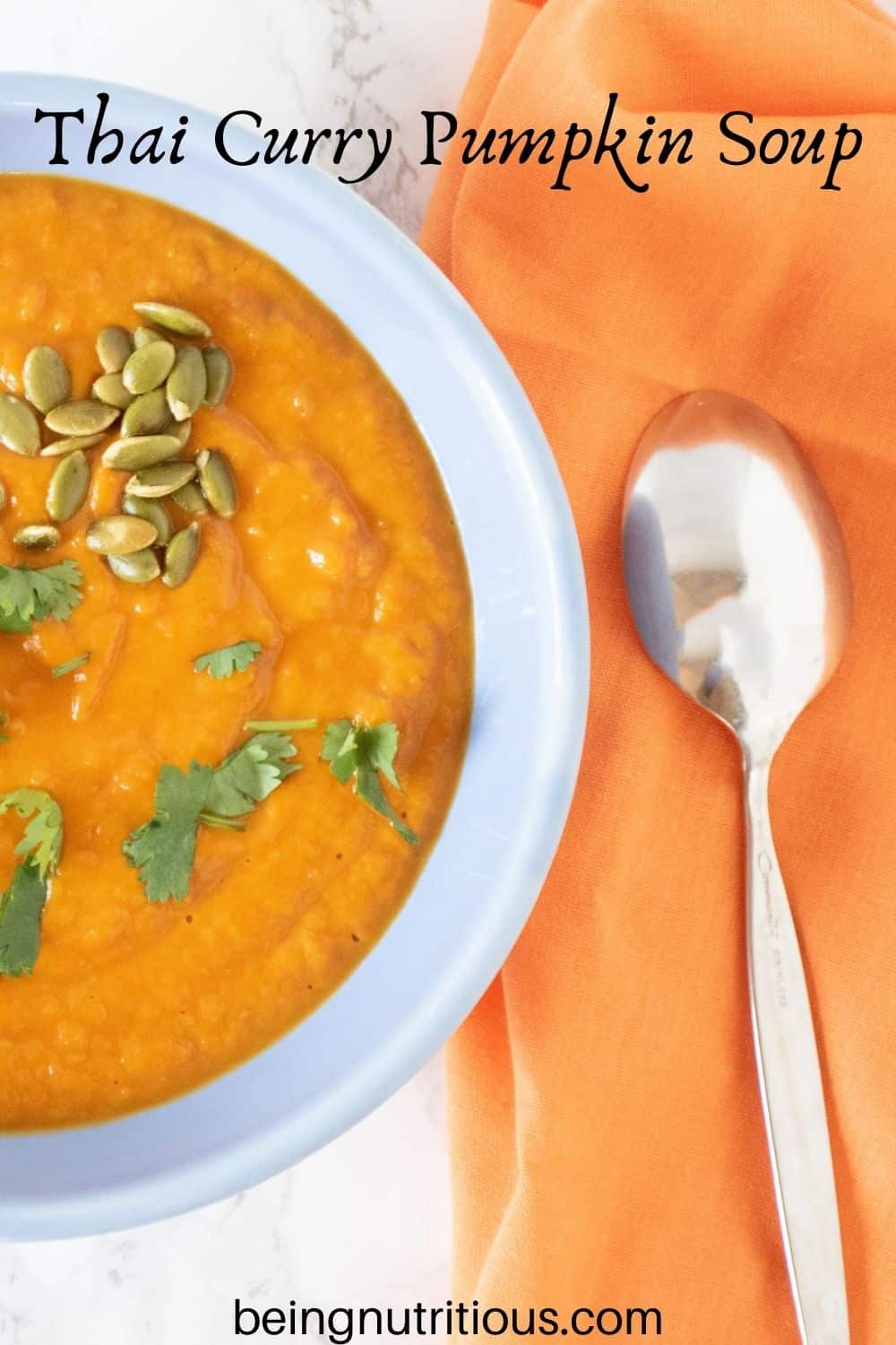 Overhead shot of pumpkin soup in a blue bowl, garnished with cilantro and pepitas. Text overlay: Thai Curry Pumpkin Soup