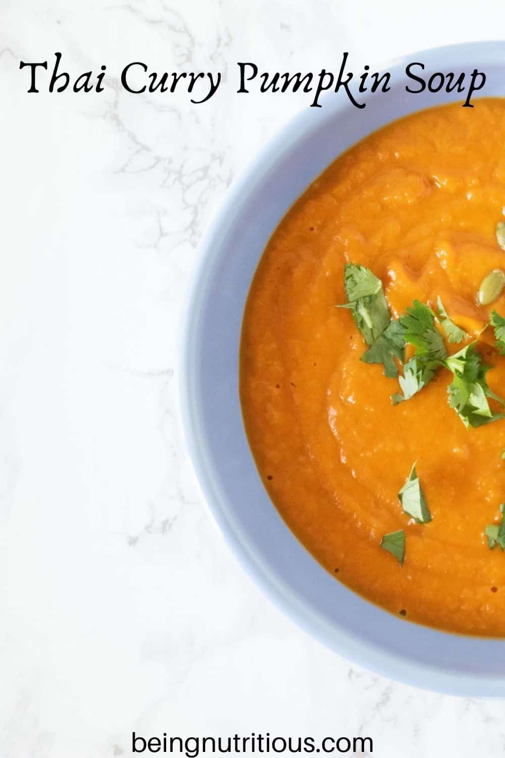 Overhead shot of half the bowl of pumpkin soup in a blue bowl, garnished with cilantro and pepitas. Text overlay: Thai Curry Pumpkin Soup
