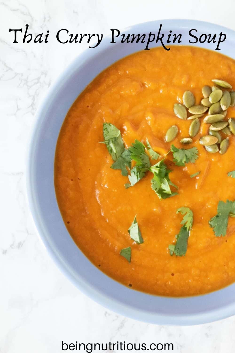 Overhead shot of pumpkin soup in a blue bowl, garnished with cilantro and pepitas. Text overlay: Thai Curry Pumpkin Soup