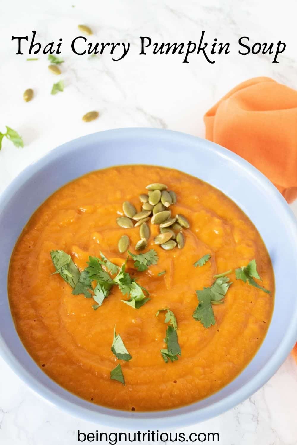 Overhead shot of pumpkin soup in a blue bowl, garnished with cilantro and pepitas. Text overlay: Thai Curry Pumpkin Soup